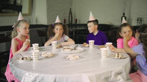 Children Have Fun Eating Birthday Cake in Festive Caps Talking and Laughing in a Cozy Festive