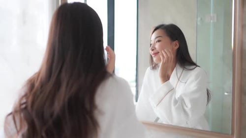 While looking in a mirror, a woman examins her healthy skin.