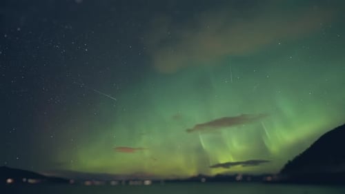 Northern lights above the fjord. Street and car lights flash in the background. Timelapse.