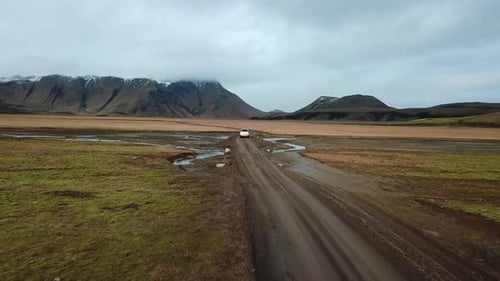 Landscape of Iceland, Aerial View of Vehicle Moving on Muddy Road in Valley Under Volcanic Mountains