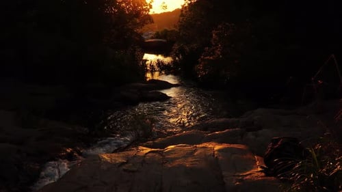 Coucher de soleil sur un ruisseau serein, lumière dorée qui brille sur les rochers à l'ombre des arbres