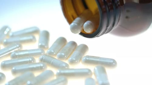 Capsules falling from amber bottle in bright light