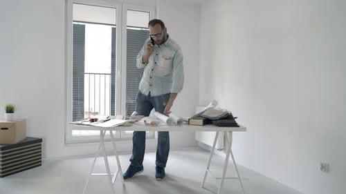 Man on Phone Examines Building Plans Indoors