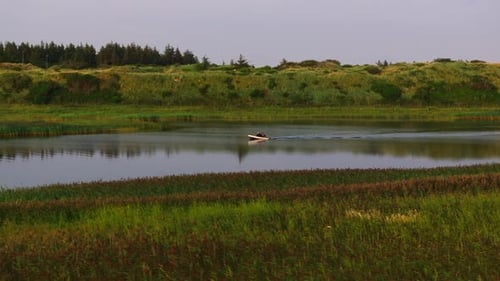 Small Fishing Boat Crosses a River at Sunset with the Warm Glow of a House Reflecting on the