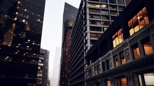 El anochecer cae sobre imponentes estructuras urbanas con ventanas brillantes y un horizonte lejano y brumoso