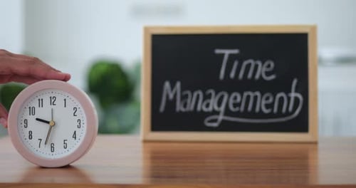 Round Clock Standing on Table Near Wooden Board with Slogan About Time Management Close Up Movie