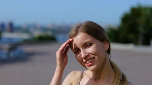 Bella dama feliz que se cubre la cara del sol con la mano mientras está de pie al aire libre en un soleado día de verano