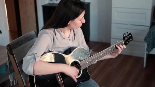 Woman Sitting Down Playing Acoustic Guitar in Home