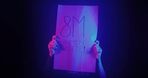 Woman Holds Up a Protest Sign in Dramatic Lighting