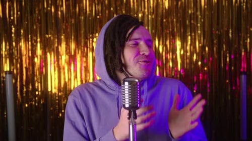 Ein gutaussehender Mann mit Dreadlocks in Freizeitkleidung hält eine Rede, eine Standup-Show, die auf einem goldenen steht
