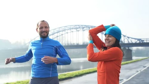 Sportive couple stretching arms by river in city warmup super slow motion