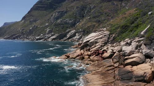 Aerial view moving along steep rocky shoreline littered with shipwreck debris in Cape Town