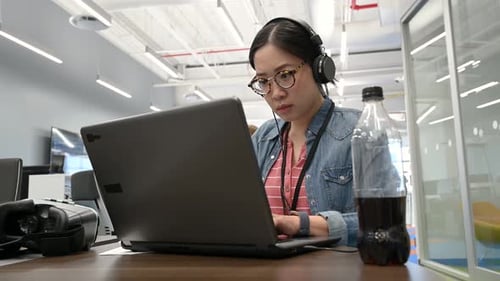 Female Computer Programmer With Headphones Working At Laptop In Office