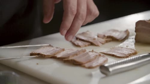 A close-up view of a professional chef carefully plating a gourmet dish using tongs. The setting is