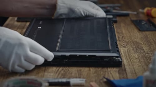 Eine Person in weißen Handschuhen interagiert mit einem Laptop auf einem Hartholztisch und zerlegt einen modernen