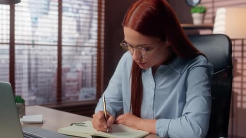 Concentrated Businesswoman with Laptop Writing Notes in Notebook Business Woman in Office Working