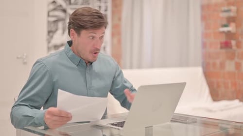 Man Reads Paperwork at Desk with Surprise