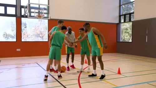 Basketball players practicing dribbling skills with coach in indoor gym