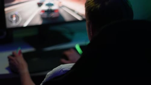 Nahaufnahme eines nicht erkennbaren männlichen Spielers, der ein Renn-Videospiel auf einem Desktop-Computer im Dunkeln fährt