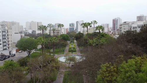 Drone 4k video Drone flies forward and up in a park revealing many trees, a fountain, and many build