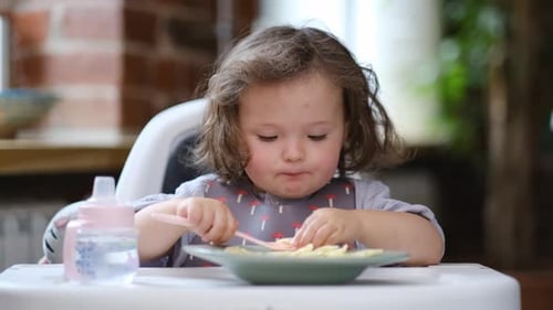 Child Eating Pasta at Table in Highchair