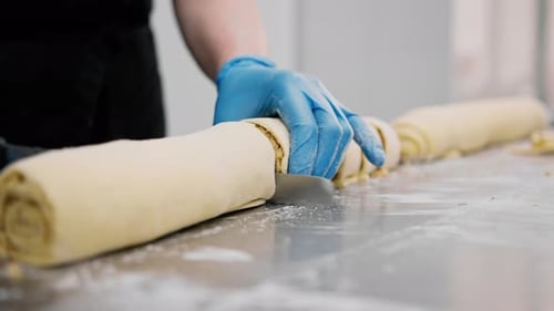 Die Küche in der Bäckerei - der Prozess der Zimtherstellung, die Bäckerin schneidet den Teig