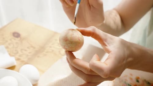 Woman carefully painting a pastel Easter egg, adding the finishing touches to the decoration.