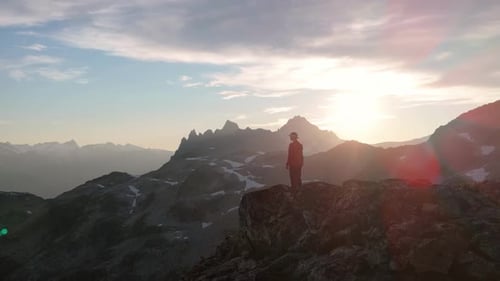 Adventurer Standing on a Mountain Peak in British Columbia Enjoying the Golden Hour Sunset.