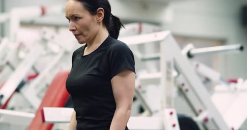 A Fit Middle Aged Woman Training Biceps with Dumbbells During an Intense Gym Workout