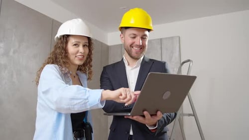 young man and woman in helmet choose room design on computer during an indoor renovation