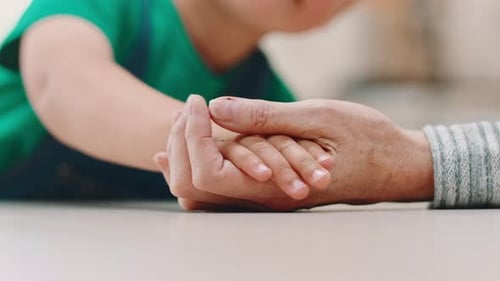 Child Gently Holds Senior Adult's Hand Indoors