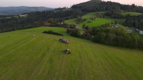 Aerial view of agricultural machinery harvesting crops in hilly landscape.