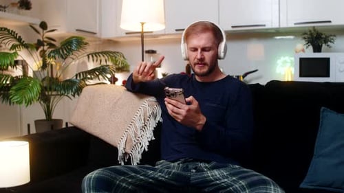 Man Listens to Music, Sits on Couch with Phone