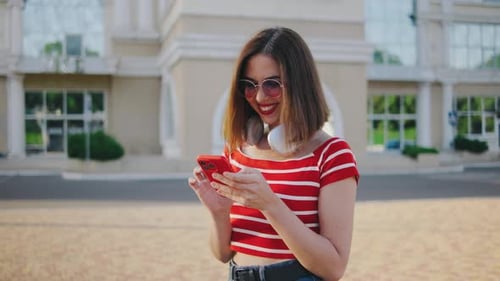 Beautiful Young Woman Uses a Smartphone on the Street Portrait of a Beautiful Girl with Headphones