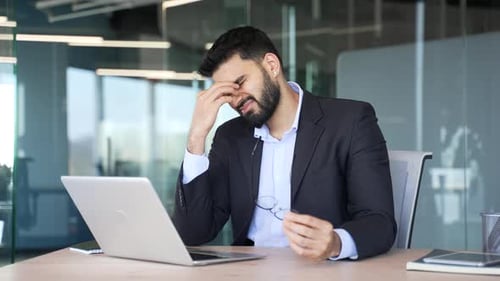 Tired Businessman Rubbing Eyes at Office Desk