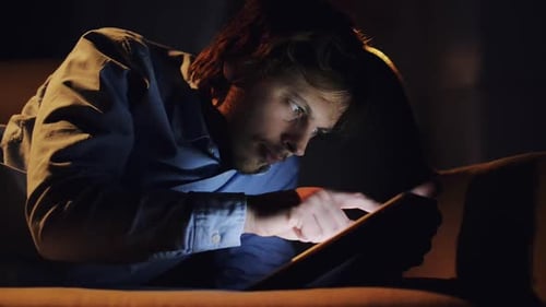 Man Relaxes on Sofa Using Tablet in Dark Room