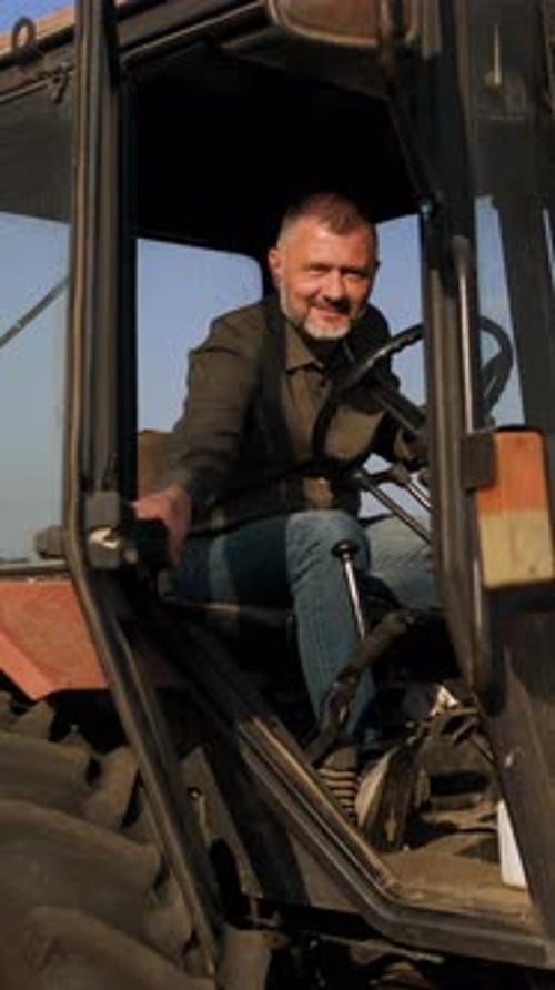 Portrait of satisfied farmer sitting in a tractor preparing to drive.