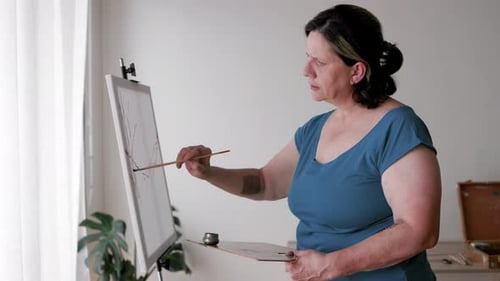 Senior artist woman painting on canvas inside home studio. Art school and craft activity