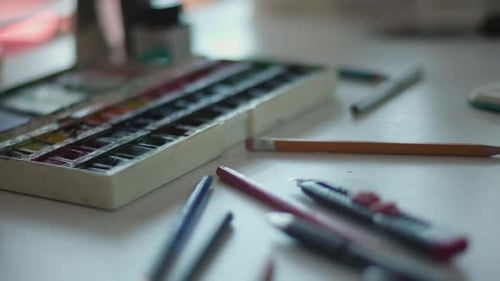 Aquarellfarben, Stifte und verschiedene Künstlerwerkzeuge zieren den Schreibtisch im Studio