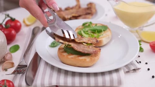 Making Egg Benedict Woman Puts Fried Bacon Onto Grilled Bun with Arugula Leaves