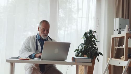 Médico senior trabajando en una computadora portátil en el escritorio de la oficina en la práctica médica