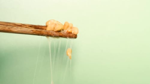 Wooden chopsticks with Japanese natto beans on green background, side view.