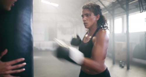 4k video footage of an attractive young female boxer training with her coach in the gym