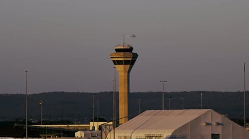 Blick auf den Sonnenuntergang auf einen Kontrollturm an einem Flughafen mit Flugzeug, das sich zur Landung nähert