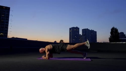 Man Does Plank Exercise on Urban Rooftop at Dusk