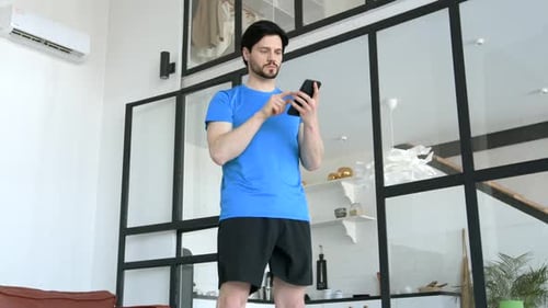 Man Doing Squats While Looking at Mobile Phone