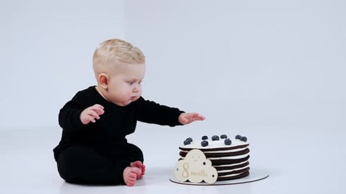 Infant Sits Next To Cake on White Floor