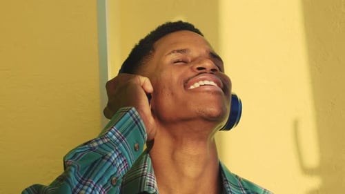 Man Enjoys Music With Headphones Against Yellow Wall
