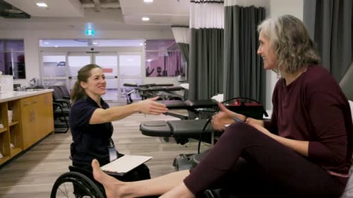 Female physical therapist in wheelchair warmly greet senior patient in clinic