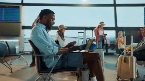 Un homme travaillant sur son ordinateur portable à l'aéroport, avec des voyageurs en arrière-plan